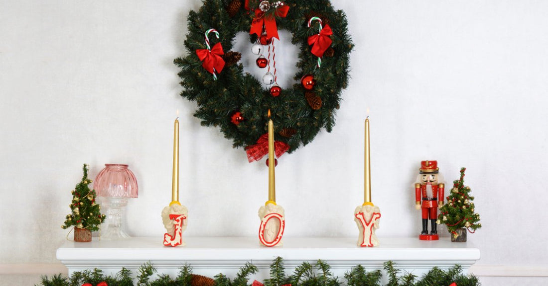 A fireplace mantel is decorated with garland, red bows, gold taper candles, miniature Christmas trees, and a nutcracker.