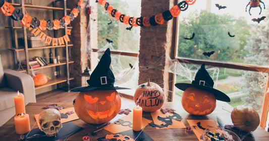 Three decorated pumpkins on a table with black and orange paper, candles, and a candy bowl. Behind them is a Halloween garland.