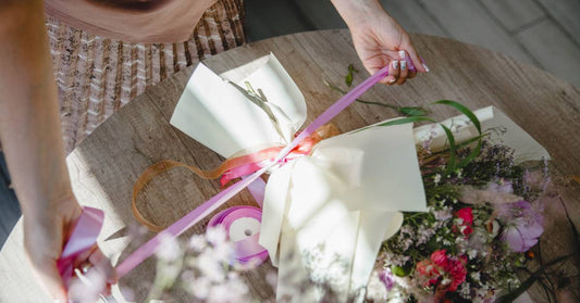 A top view of someone tying a ribbon around a beautiful bouquet of flowers. The bouquet is also wrapped in a white cloth.