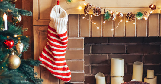 A striped Christmas stocking is hanging from a fireplace mantel. A decorated Christmas tree is next to the stocking.