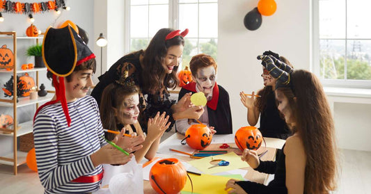 A classroom of kids in costumes is standing around a table doing a craft with their teacher. Fall decor is everywhere.