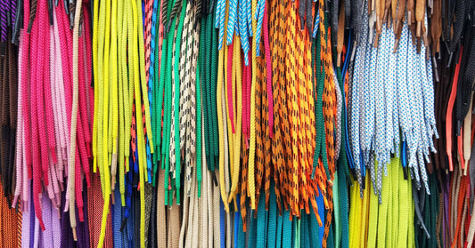 A large quantity of shoelaces in various colors and patterns hanging vertically, with matching colors bunched together.