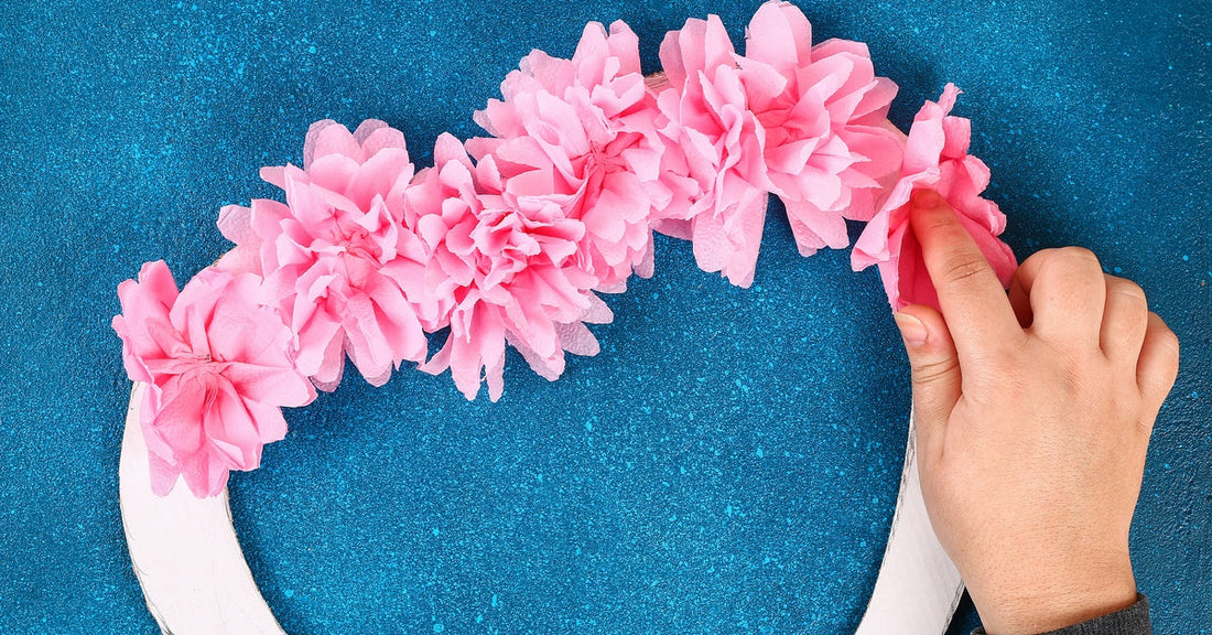 Someone places light pink paper flowers along the base of a wreath. The wreath is in the shape of a heart.