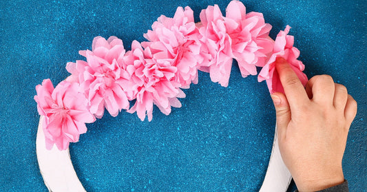 Someone places light pink paper flowers along the base of a wreath. The wreath is in the shape of a heart.
