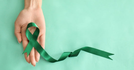 Someone holds a green awareness ribbon in their palm, with the ribbon trailing off onto a light green background.