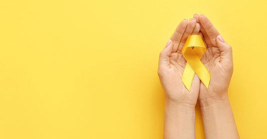 Someone cups a yellow awareness ribbon in the palm of both of their hands. Their hands rest on a yellow background.