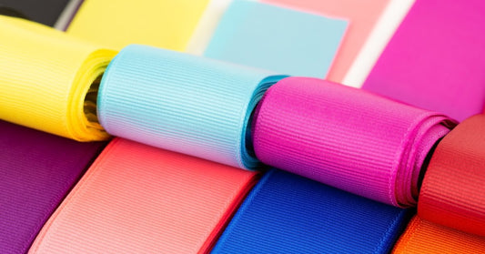 A close-up of brightly colored, thick grosgrain ribbons. Yellow, blue, pink, red, orange, and purple colors are present.