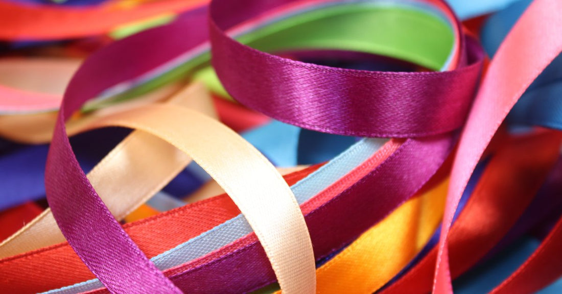 A pile of different colored satin ribbons. Some are a magenta color, while others are red, yellow, baby blue, and more.
