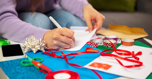 A woman sits in front of a table with lots of different crafting supplies, including ribbon, washi tape, paper, and scissors.