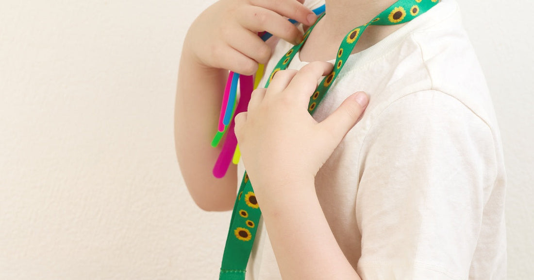 A close-up of a child wearing a lanyard made from green ribbon. Small sunflowers decorate the ribbon lanyard.