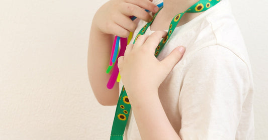 A close-up of a child wearing a lanyard made from green ribbon. Small sunflowers decorate the ribbon lanyard.
