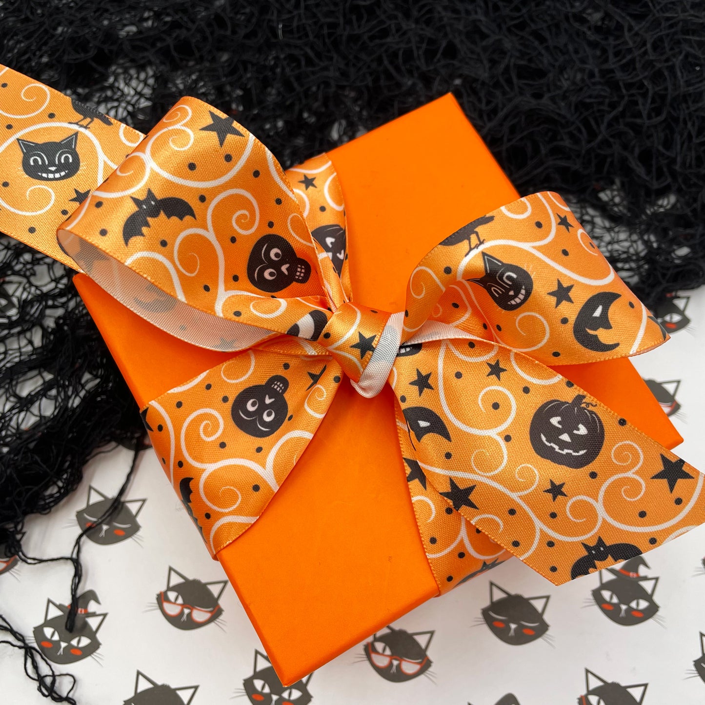 Vintage Halloween ribbon featuring black cats, jack o'lanterns, bats, stars and moons printed on an orange background with cream swirls on white satin